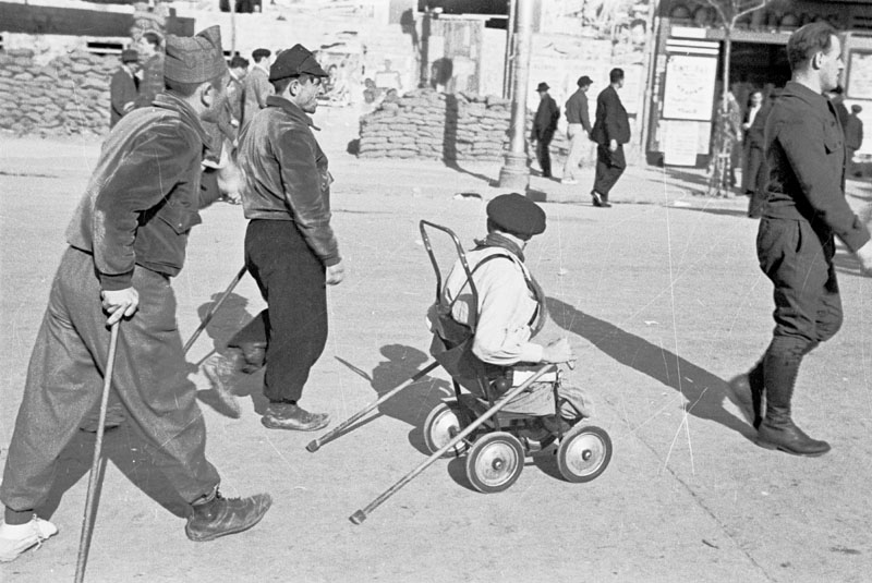 Soldados heridos descansan en la retaguardia, en primer plano aparece uno de ellos con las piernas amputadas y montado en un carrito.